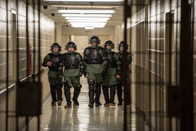 ICE team in riot gear walking through a detention facility